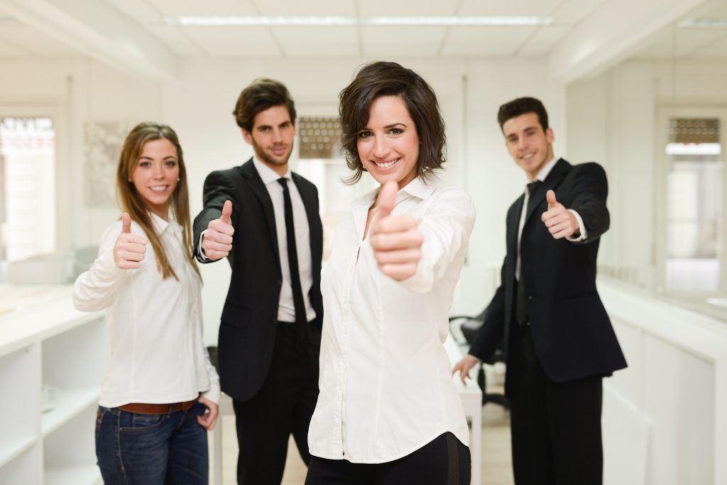 Cheerful business team giving thumbs up with young woman leader in center